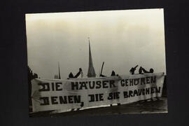 Foto Leute mit Transpi «Die Häuser gehören denen, die sie brauchen» ev. auf Polyterrasse